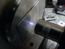 
   
    Figure 26 : Exemple d'usinage d'une plaque métallique par un laser picoseconde : la lumière qui apparaît est un plasma dû à l'éjection de la matière. La plaque métallique à usiner est sur la gauche.
   
  